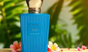 Niebieska butelka perfum Lou de Pre Paradis Vanille z złotą nakrętką, otoczona tropikalnymi kwiatami i liśćmi.