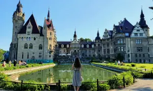 Kobieta podziwia zamek Moszna, jedną z największych atrakcji Opolszczyzny. Wspaniała architektura i staw tworzą malowniczy widok.