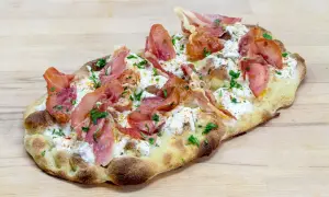 Une délicieuse pinsa recette garnie de burrata crémeuse, de fines tranches de prosciutto et de persil frais, le tout sur une pâte dorée.