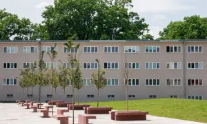 Nowoczesny budynek mieszkalny w stylu wuwa Wrocław z rzędem drzew i betonowych ławek przed fasadą.