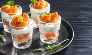 Quatre verrines apéro garnies de crevettes et d'une crème onctueuse, décorées de persil frais.