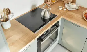 Un bollitore d'acciaio su un piano cottura a induzione in una cucina senza cappa. Utensili in legno in un contenitore.