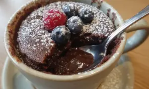 Chokladig mug cake med bär och florsocker. En sked dyker ner i den smältande chokladen.