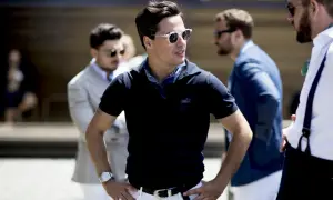 Ein Mann in einem dunkelblauen Poloshirt mit weißem Gürtel und weißer Hose, dazu ein blaues Halstuch. Ein stilvolles Outfit für Herren.