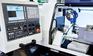 Panel sterowania zaawansowanych maszyn CNC z ekranem, klawiaturą i pokrętłami. Widać fragment obrabianego detalu i system chłodzenia.