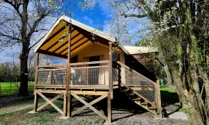 Un lodge de camping éco-responsable avec une tente surélevée et une terrasse en bois, entouré d'arbres fleuris sous un ciel bleu.
