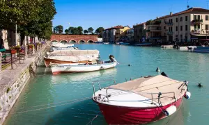 Barche ormeggiate nel canale, un assaggio di cosa vedere a Peschiera del Garda. Edifici colorati e un ponte ad arcate sullo sfondo.