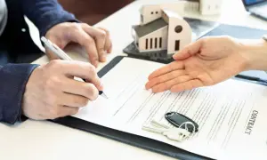 Signature d'un contrat immobilier. Un homme signe un document, des clés et un modèle de maison sont posés sur la table. Le courrier sru est prêt.