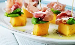 Melonbitar med prosciutto och basilika på ett fat. En klassisk och läcker kombination.