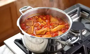 Un délicieux saute de porc mijote dans une cocotte en acier inoxydable sur une cuisinière à gaz, dégageant une vapeur appétissante.