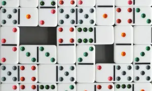 Wiele białych kostek do gry w domino z kolorowymi kropkami (zielonymi, czerwonymi, szarymi i pomarańczowymi) ułożonych w rzędy.