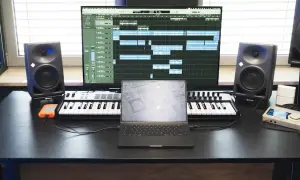 Studio do nagrywania muzyki: monitory studyjne, klawiatury MIDI, laptop i ekran z sekwencerem.