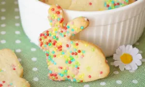 Bunte Osterkekse zum Ausstechen, verziert mit bunten Streuseln, liegen auf einem grünen Tupfentuch. Ein süßer Osterhase steht im Vordergrund.