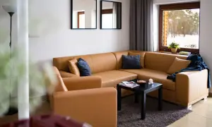 Przytulny salon z brązową kanapą i fotelem, z widokiem na zimowy las. Idealne miejsce na odpoczynek, jak w **starej wsi**.