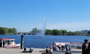 Ein sonniger Tag am Alstersee Hamburg. Menschen entspannen sich am Ufer, während die berühmte Fontäne in die Höhe schießt.