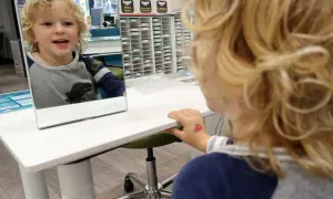 Chłopiec z blond włosami patrzy w lustro, uśmiechając się.