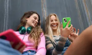 Dwie uśmiechnięte dziewczyny rozmawiają przez **Facetime** na telefonach, jedna z nich trzyma zielony smartfon.