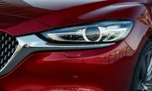 Błyszczący, czerwony lakier Mazda 6 Skyactiv odbija otoczenie. Widoczny fragment reflektora i chromowana atrapa.
