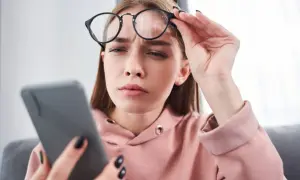 Zmarszczona kobieta w okularach trzyma telefon, szukając domowych sposobów na mroczki przed oczami.