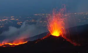 Spektakularna erupcja Etny nocą. Wulkan wyrzuca strumienie lawy i iskier na tle rozświetlonego miasta.