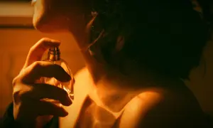 Kobieta aplikuje perfumy. Czy to zapach gourmand? Ciepłe światło podkreśla jej szyję i ramię.