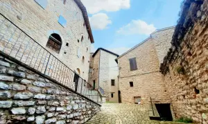 Antica via acciottolata a Caldarola, Marche, con edifici in pietra e cielo azzurro.