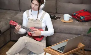 Dziewczyna w słuchawkach uczy się grać na ukulele, zastanawiając się, ile trwa nauka gry na gitarze.