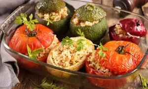 Un plat de petits farcis gastronomiques : tomates, courgettes rondes et oignons rouges farcis de grains et herbes, dans un plat en verre.