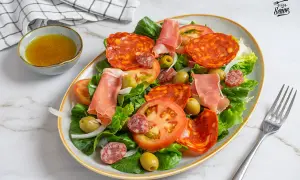 Una fresca ensalada catalana con lechuga, tomate, aceitunas, chorizo, salchichón y jamón serrano.