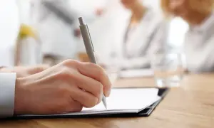 Dłoń pisze długopisem na dokumencie, finalizując umowę cywilnoprawną.