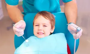 Mały pacjent u dentysty, który bada ząbki. Warto wiedzieć, co na ból zęba u dziecka, by szybko ulżyć maluchowi.