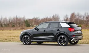 Czarne Audi Q2 z białym akcentem na słupku C, zaparkowane na tle jesiennego krajobrazu. Wiele osób szuka audi q2 opinie przed zakupem.