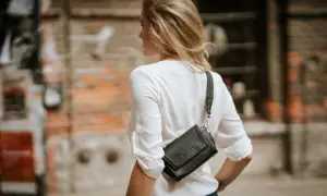 Blondynka w białej bluzce nosi czarną torebkę na ramieniu. Wygląda jak modna bimbo, gotowa na spacer po mieście.