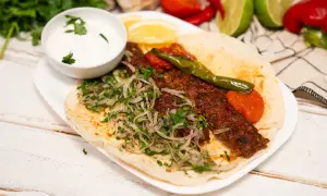 Domowy kebab z mięsem, cebulą, pietruszką, pomidorami i sosem jogurtowym na placku.