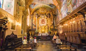 Wnętrze sanktuarium pasyjno-maryjnego w Kalwarii Zebrzydowskiej. Złoty ołtarz, malowidła na ścianach i sklepieniu, wierni na ławkach.