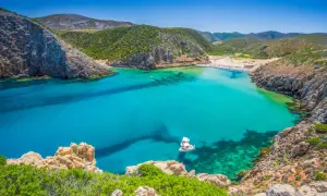 Traumhafte Cala Domestica mit türkisfarbenem Wasser, Felsen und grünen Hügeln. Ein Boot ankert in der Bucht.