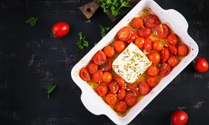 Tomates cerises au four, tendres et juteuses, baignant dans leur jus avec un bloc de feta crémeuse. Un délice simple et savoureux.