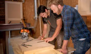 Carpinteros trabajan con madera calabo en un taller. Uno marca una pieza de madera mientras el otro observa.