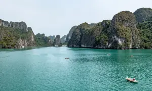 Wody Zatoki Ha Long, gdzie historia Wietnamu splata się z legendami. Małe łódki i statki przemierzają turkusowe morze między wapiennymi wyspami.