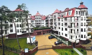 Elegancki budynek w stylu alpejskim, przypominający Continental Hotel Krynica, z białymi fasadami, czerwonymi dachami i drewnianymi elementami.