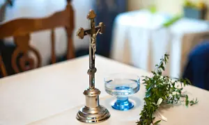 Krzyż, kropielniczka z wodą i gałązka bukszpanu na stole. Symbolika błogosławieństwa młodej pary.