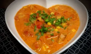 Pyszna zupa gyros z kawałkami kurczaka, kukurydzą i pomidorami, posypana szczypiorkiem.
