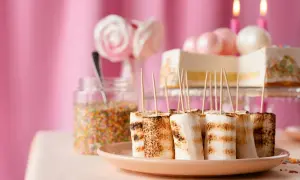 Grillade marshmallows på spett, perfekt fika till barnkalas. En tårta och strössel i bakgrunden.
