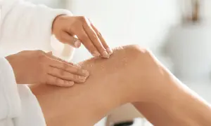 Mani che applicano scrub corpo sulla gamba, mostrando come si usa per una pelle liscia e luminosa.