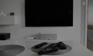 Na stole leży kilka pilotów, gotowych do obsługi czarnego ekranu telewizora wiszącego na ścianie.