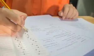 Dłoń z ołówkiem zaznacza odpowiedzi na arkuszu egzaminacyjnym.