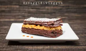 Un goloso millefoglie al cioccolato, con strati croccanti e crema dorata, spolverato di zucchero a velo.