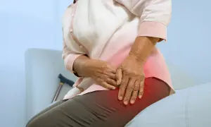 Une femme âgée se tient la hanche, souffrant de mal de hanche et sciatique. Une canne est visible derrière elle.