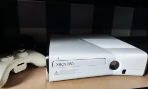 Biała konsola Xbox 360 i kontroler na półce.