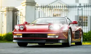 Czerwone Ferrari Testarossa z podnoszonymi światłami, zaparkowane przed elegancką posiadłością.